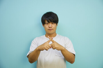 青背景の前でバツを作るアジア人男性	