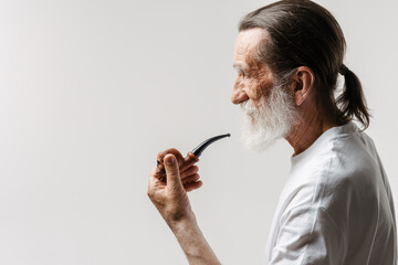 European senior man looking aside while posing with smoking pipe