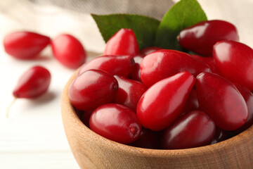 Fresh ripe dogwood berries with green leaves in bowl on white table, closeup