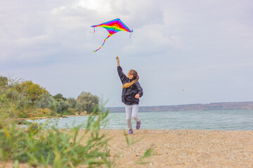 a teenage girl runs with a bright multi-colored kite along the shore of a pond. concept of outdoor activities and a healthy lifestyle.