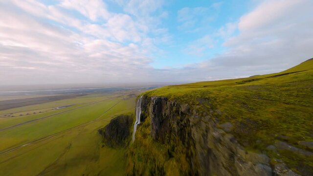 FPV drone shot diving down a waterfall, in partly sunny Esjan mountains, Iceland