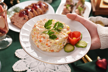 A hand holding a plate with vegetable salad for Christmas to put on festive table