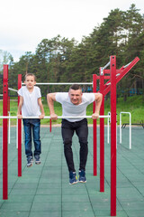 Fototapeta premium Caucasian man trains a boy on the uneven bars on the playground. Dad and son go in for outdoor sports.
