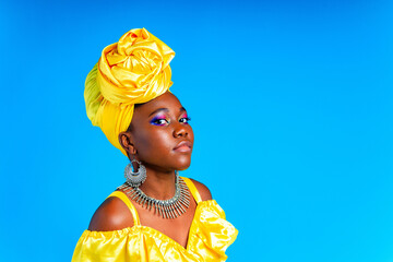 African woman with yellow silk turban and silver earrings and nose piercing in blue studio...