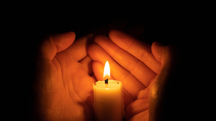 Two hands holding burning candle in darkness, closeup