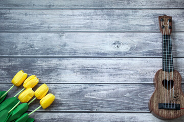 Top view, yellow tulips on original wooden textured table, a guitar, copy space
