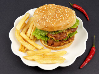 Closeup of a hamburger, french fries, red peppers on the black table