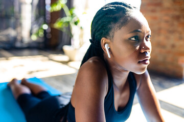 african american woman in black sporty bra is making yoga on mat floor and listening an audio...