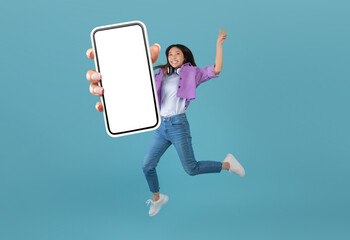 Excited asian lady showing empty smartphone screen while jumping up over blue studio background, collage, banner