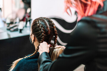Woman at hairdresser getting her hair done in braids by a pink hair lady at the salon