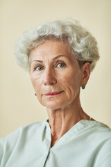 Vertical portrait of elegant senior woman looking at camera against neutral background