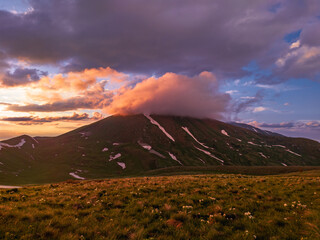 A beautiful cloud illuminated by orange light descends from the top of the mountain during sunset....