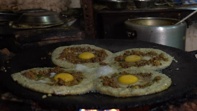 Frying Newari bara with eggs and meat on a skillet over a fire.