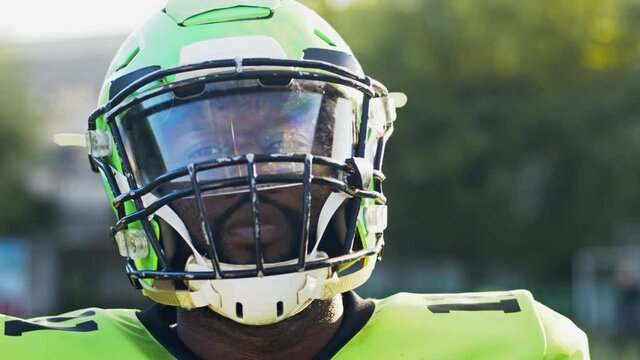 Portrait view of the American football player wearing helmet looking at the camera after training. Male person in uniform during the game. Sport concept