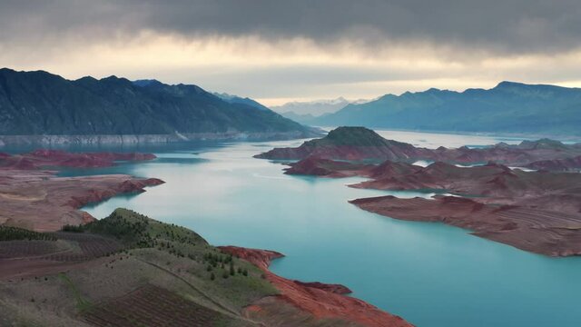 Aerial flight Beautiful spring landscape of river with blue turquoise water and hills against background of mountains and dawn sky. Bare rocky shores are visible due to ow water level on the lake.
