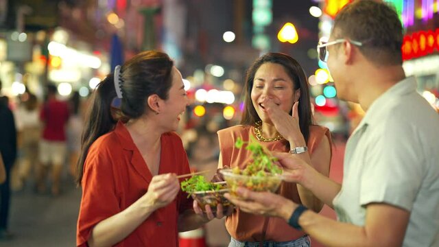 4K Group of Asian woman and LGBTQ people friends tourist enjoy eating traditional street food bbq seafood grilled squid with spicy sauce together at china town street night market in Bangkok, Thailand
