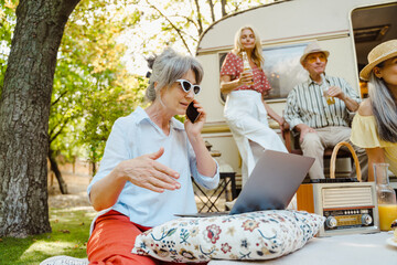 Senior woman talking on cellphone while having picnic with her friends