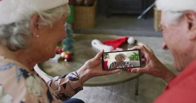 Senior caucasian couple using smartphone for christmas video call with smiling friend on screen