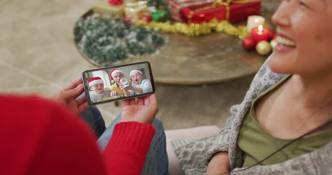 Smiling asian couple using smartphone for christmas video call with family with santa hats on screen