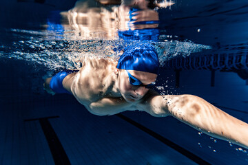 Professional male swimmer in swimming cap and goggles in motion and action during training at pool, indoors. Healthy lifestyle, power, energy, sports movement concept