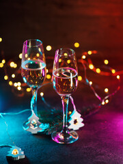 Two glasses of sparkling wine, neon background and bokeh garlands.