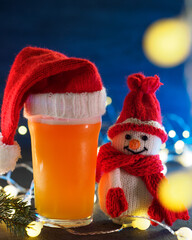 happy snowman and a glass of Christmas beer ale in a Santa Claus hat. Blue background, garland