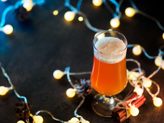 A glass of Christmas beer ale on a dark background with a side garland and copyspace. Craft seasonal limited beer