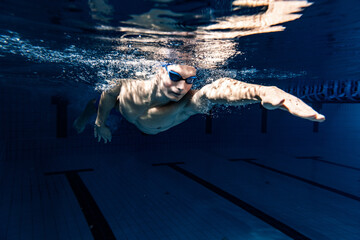 Close-up. Young male swimmer in swimming cap and goggles in motion and action during training at pool, indoors. Underwater imaging