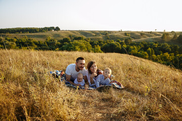Fototapeta na wymiar a family with small children on a background of tall grass lies on a calety blanket