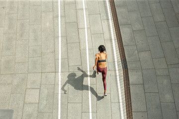 Young biracial woman in stylish sportswear runs along empty stadium track upper view. Development and achievement concept