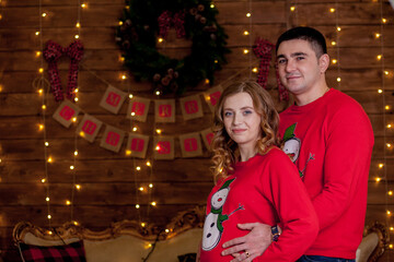 Close up of happy married couple bonding next to Christmas tree. Best Christmas gift. Young pregnant woman with her husband decorate the Christmas tree. A young loving couple in cozy sweaters