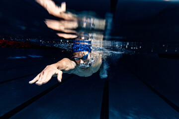 Close-up. Young male swimmer in swimming cap and goggles in motion and action during training at...