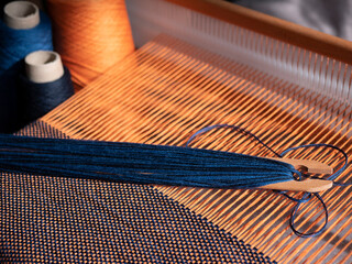 Creation of the blue and orange textile using weaving loom. Wooden loom, shuttle and cones with...