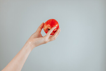 Female hand is holding red apple on a grey background. Minimal fruit concept. Fruit nutrition concept