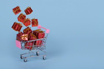 Minimal Christmas sale composition. Shopping cart or trolley with flying  gifts on a blue background.