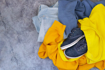 clothes on blue background: jeans blue sweater yellow hoodie sneakers. Top view