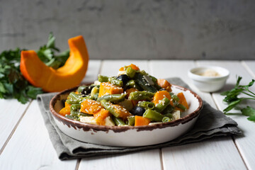 Delicious breakfast: salad of baked pumpkin, string beans and cheese on a white plate on a white wooden table. Close-up