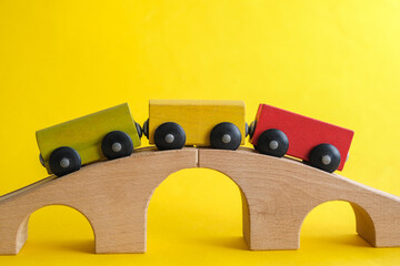 Toy, yellow, green, red wooden trailers stand on a wooden bridge, on a yellow background. Close-up. Horizontal photo