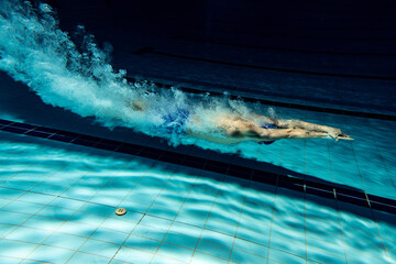 Underwater camera work. One male swimmer training at pool, indoors. Underwater view of swimming movements details.