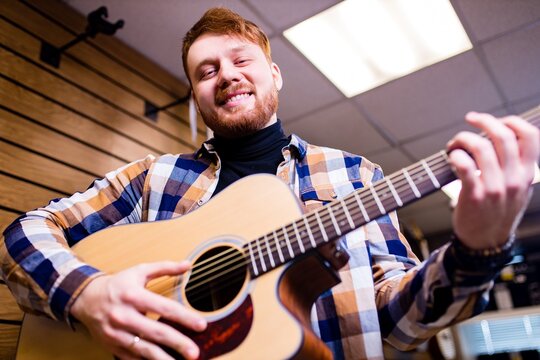 Man with red ginger hair and beatd is considering a guitars in a music store