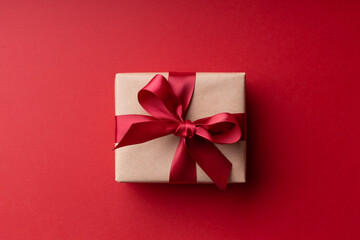 Top view on Christmas gift box with red bow on red background.
