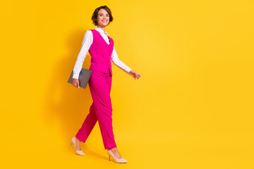 Fototapeta na wymiar Photo of shiny adorable young lady wear pink suit holding modern device walking empty space smiling isolated yellow color background
