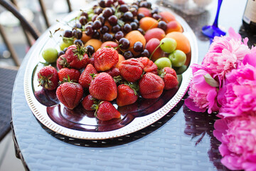 Pink peony rose flower, peaches, cherries and sweet strawberries on a tray. Beautiful Still life on the terrace on the table. top view.
