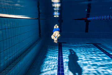 Underwater shooting. One male swimmer training at pool, indoors. Underwater view of swimming...