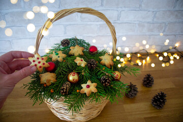 Fototapeta na wymiar selective focus on hand holding delicious handmade snowflake-shaped homemade cookies against blurry speck of lights garlands and christmas basket with fir branches