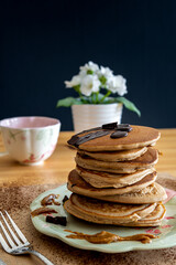 Healthy buckwheat pancake stack with dark chocolate, maple syrup and halvah on a decorative plate. Easy to make gluten free morning breakfast or brunch. Delicious heap of golden pancakes with teacup.