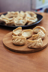 Uncooked russian pelmeni on cutting board and ingredients for homemade pelmeni on white table. Process of making pelmeni, ravioli or dumplings with meat