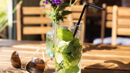 a beautiful iris in a glass vase, next to a glass of mojito on a dark background of a brown wooden table in a cafe on the summer veranda