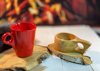 on the wooden table by the fireplace are wooden coasters and a red mug and a wooden cup