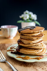 Healthy buckwheat pancake stack with dark chocolate, maple syrup and halvah on a decorative plate. Easy to make gluten free morning breakfast or brunch. Delicious heap of golden pancakes with teacup.